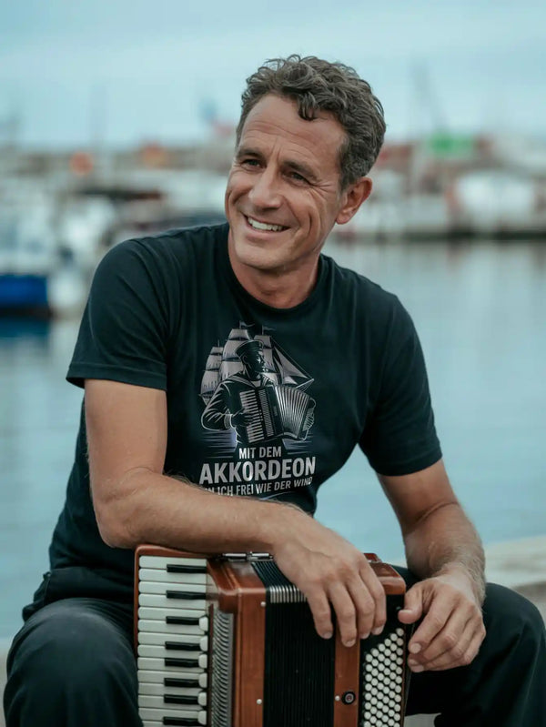 Akkordeonist mit T‑Shirt „Mit dem Akkordeon frei wie der Wind“ am Hafen
