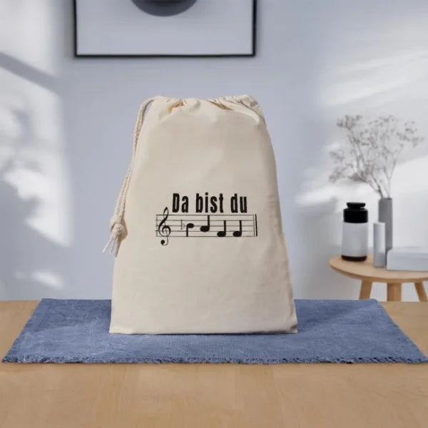 Naturfarbener Geschenkbeutel mit dem Notenschrift-Motiv „Da bist du baff“ in einer hellen Wohnszene.