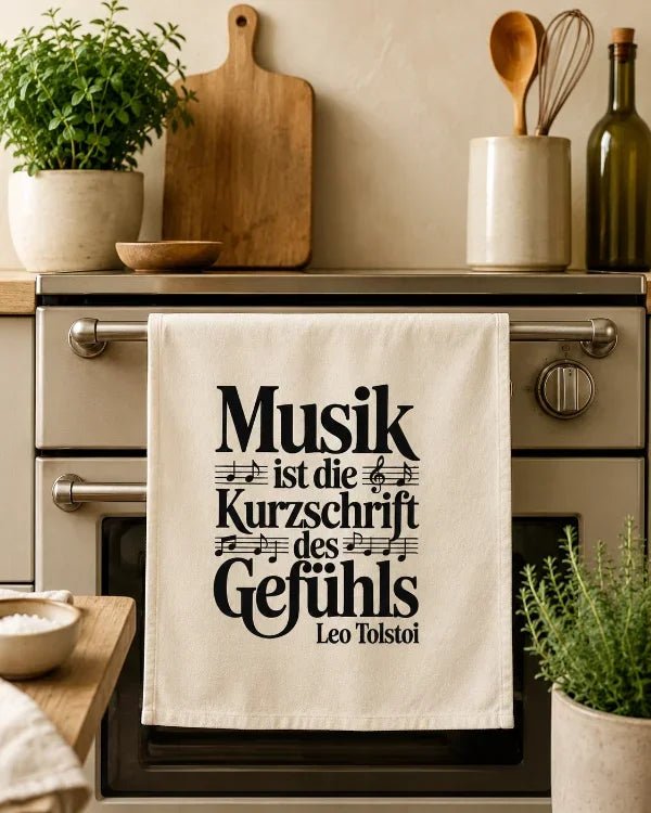 Naturfarbenes Geschirrtuch mit dem Musikzitat „Musik ist die Kurzschrift des Gefühls“ in einer Küchenszene.