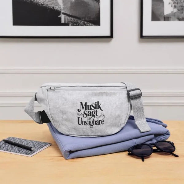 Graue Gürteltasche mit dem Zitat „Musik sagt das Unsagbare“ in einer modernen Wohn- und Schreibtischszene.