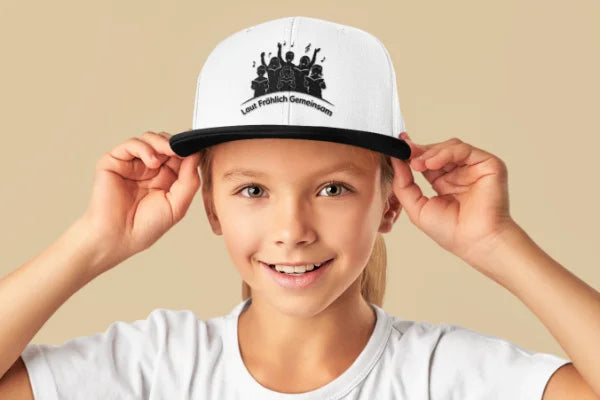 Kinder-Trucker-Cap mit Kinderchor-Motiv „Laut Fröhlich Gemeinsam“ auf einem lächelnden Kind.