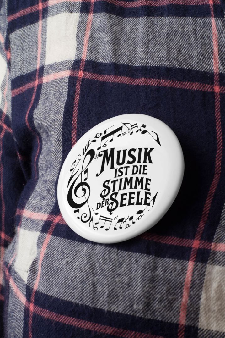 Runder Button mit dem Spruch „Musik ist die Stimme der Seele“ und Musiknoten an einem karierten Hemd