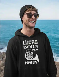 Lächelnder Mann am Meer trägt einen schwarzen Herren-Hoodie mit personalisiertem „Born to play Horn“-Design und dem Namen Lucas.
