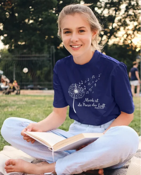 Dunkelblaues Damen-T-Shirt mit Pusteblumen- und Notenmotiv „Musik ist die Poesie der Luft“ beim Picknick im Park.