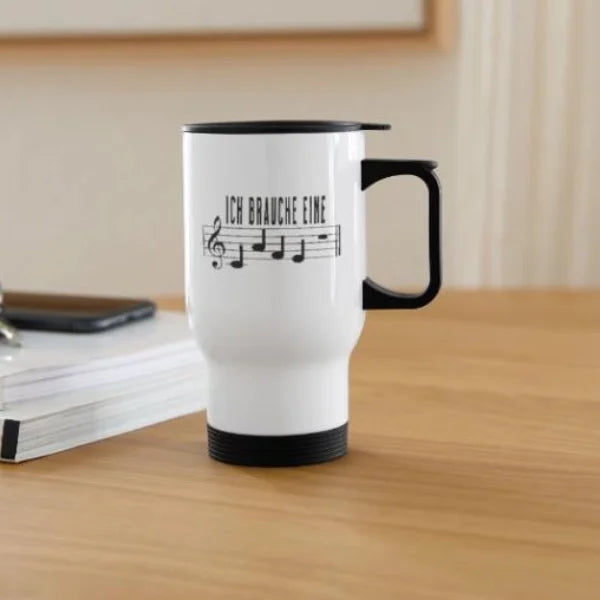 Weißer Thermobecher mit Notenschrift-Spruch „Ich brauche eine Café-Pause“ auf einem Schreibtisch.