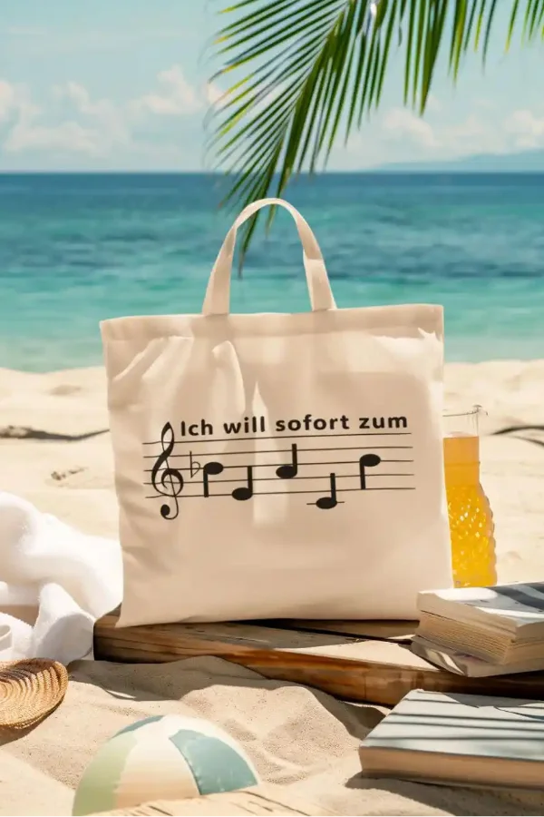 Naturfarbene Tragetasche mit dem Notenschrift-Spruch „Ich will sofort zum Beach“ in einer sommerlichen Strandszene.