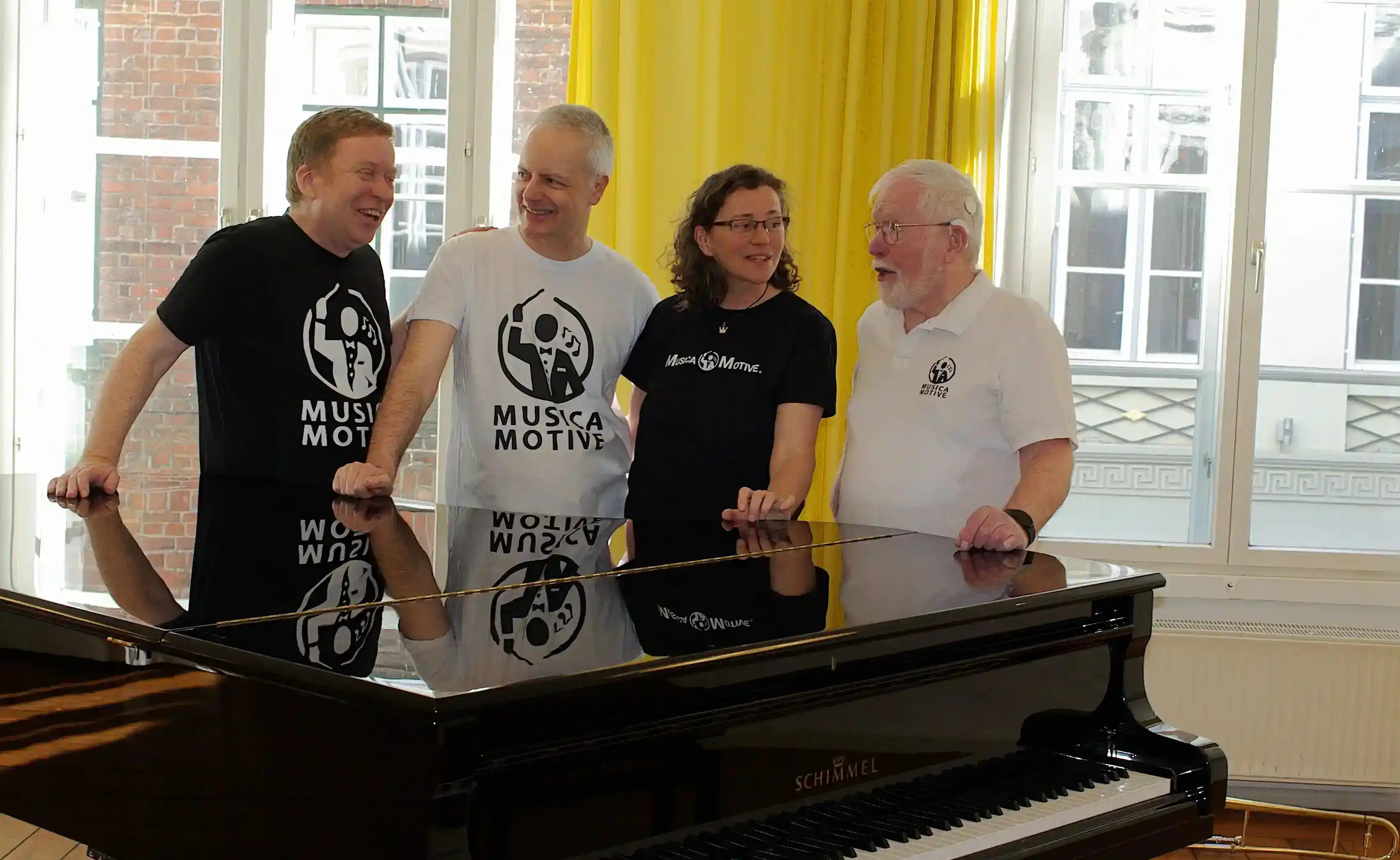 Das MusicaMotive-Team im Musikraum am Flügel in MusicaMotive-Shirts.