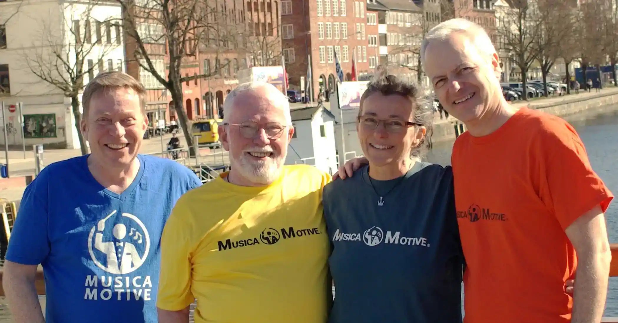 Das MusicaMotive-Team am Wasser an der Trave in Lübeck in farbigen MusicaMotive-Shirts.